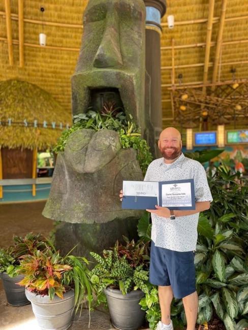 Daniel standing at Universal Studios, showing his team member of the month certificate