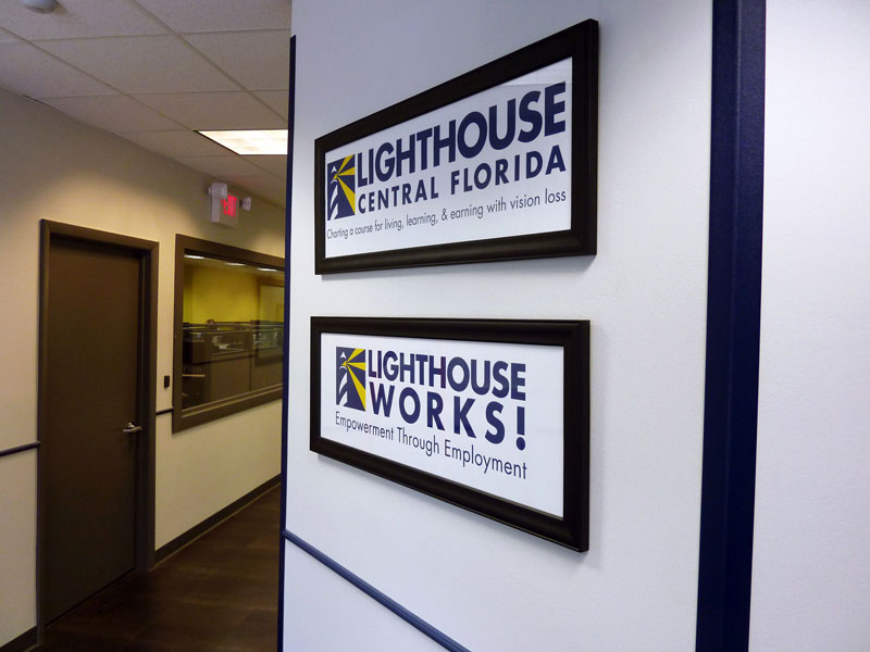 an image of a hallway leading into the Lighthouse Works building with the contact center on the left, and a wall  on the right with the Lighthouse Central Florida and Lighthouse Works logos on it