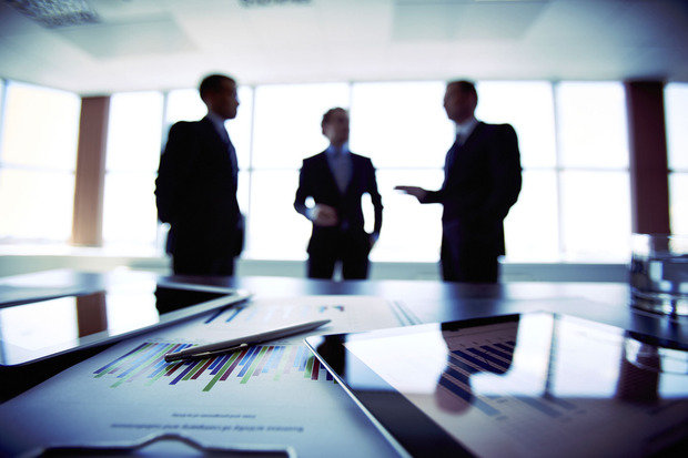 a picture a few people standing over a table of documents in a conversation