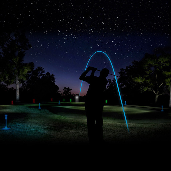 a golfer hitting a glowing ball from a tee at night